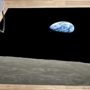 Puede incluir: Una alfombra en blanco y negro con una foto de la Tierra elevándose sobre la superficie de la luna.