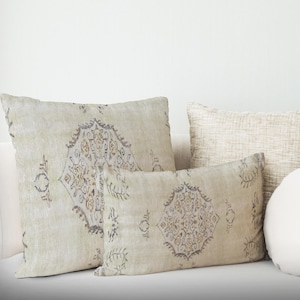 Pode incluir: Duas almofadas decorativas com fundo bege e um padrão marrom e cinza. As almofadas estão em um sofá branco.