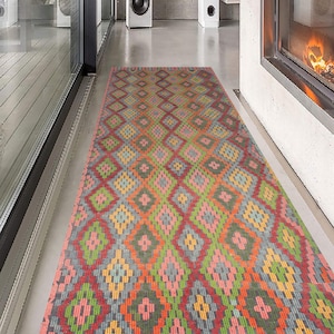 May include: A rectangular, patterned rug with a repeating diamond design in shades of red, pink, green, orange, and yellow. The rug is placed on a polished concrete floor in a modern interior setting.