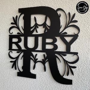 Peut inclure: Décoration murale en métal noir avec le nom "RUBY" et une décoration florale autour de la lettre "R".