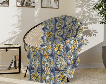 May include: A blue and white throw blanket with a lemon pattern. The blanket is draped over a chair with a woven rattan frame.