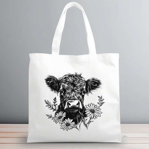 May include: A white tote bag with a black and white illustration of a cow's head with flowers. The cow is looking directly at the viewer.