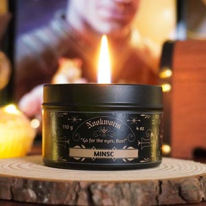 May include: A black candle tin with gold lettering that reads "Nooknorn" and "Go for the eyes, Boo!"  The candle is labeled "Minsc" and is 4 oz or 110 g.