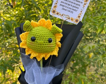 May include: A bouquet of yellow crocheted sunflowers with a green crocheted character in the center. The bouquet is wrapped in black paper with a yellow ribbon and a white tulle bow. A card with a quote from the movie Shrek is attached to the bouquet.