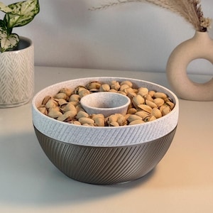 Puede incluir: Un bol de cerámica marrón y blanco con un bol blanco más pequeño en el centro. El bol está lleno de pistachos.