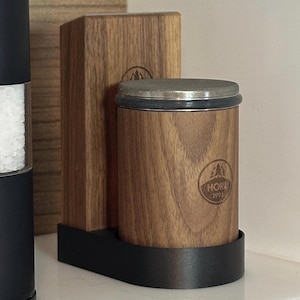 Könnte beinhalten: Ein Salz- und Pfefferstreuer-Set aus Holz mit schwarzem Sockel. Die Streuer sind aus Holz und haben einen silbernen Deckel. Die Streuer sind mit "HORK 1991" beschriftet.