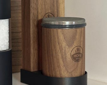 May include: A wooden salt and pepper shaker set with a black base. The shakers are made of wood and have a silver top. The shakers are labeled "HORK 1991".
