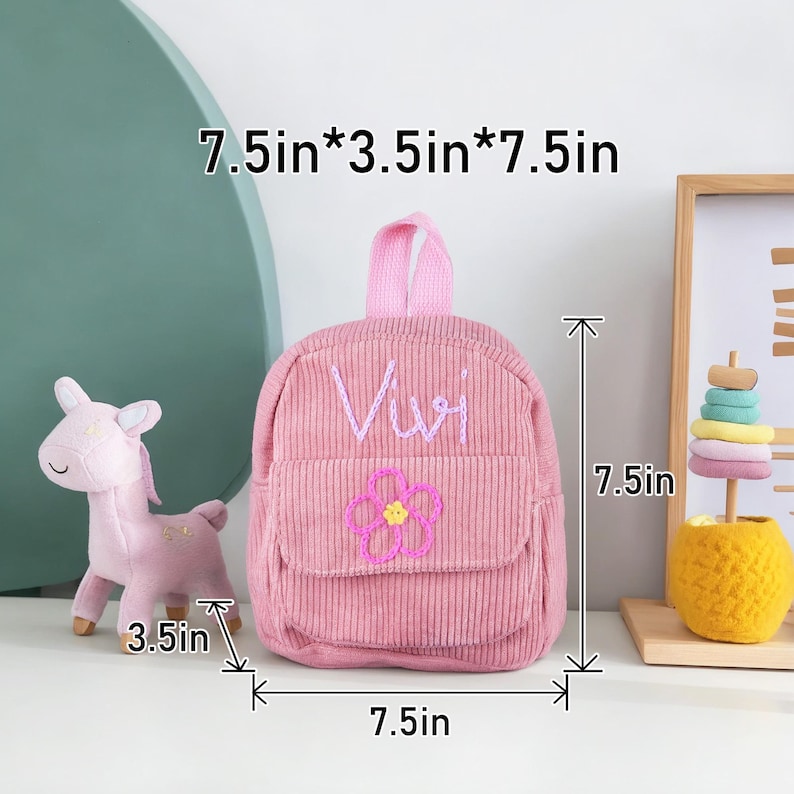 May include: Pink corduroy mini backpack with a flower and the name "Vivi" embroidered on the front. The backpack measures 7.5 inches wide, 3.5 inches deep, and 7.5 inches tall.