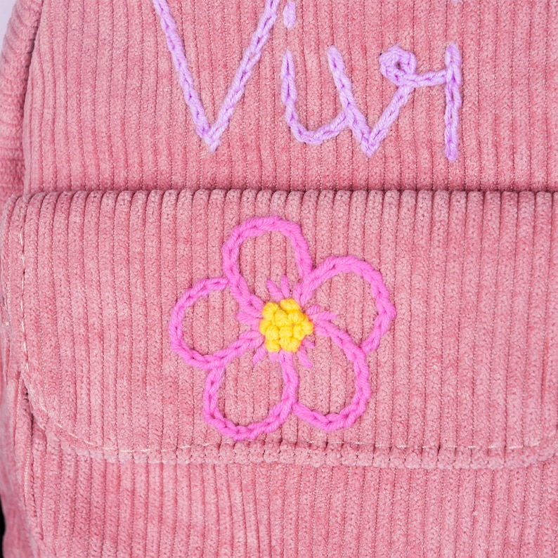 May include: Pink corduroy backpack with a flower embroidered on the front pocket and the word "Viv" embroidered on the top flap.