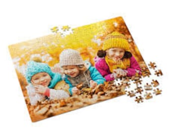 Op de afbeelding: Drie kinderen met wintermutsen en sjaals liggen op een bed van herfstbladeren. De kinderen lachen en kijken naar de camera. De achtergrond is een wazig beeld van een bos.