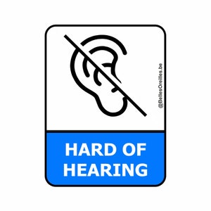 Op de afbeelding: Een wit vierkant bord met een zwarte rand en een blauwe rechthoek aan de onderkant. Het bord heeft een zwart oor met een diagonale streep erdoorheen. De tekst "HARD OF HEARING" staat in zwarte letters op de blauwe rechthoek. De tekst "@BellesOreilles.be" staat in zwarte letters aan de rechterkant van het bord.