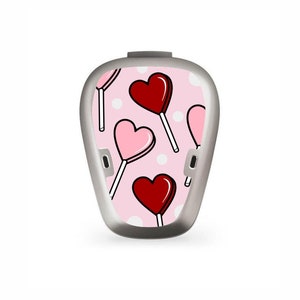 Puede incluir: Una piel con estampado rosa y blanco con un diseño de piruleta en forma de corazón para un dispositivo médico.