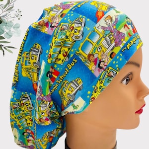 May include: A blue and yellow scrub hat featuring a print of the Magic School Bus and characters from the show. The text "The Magic School Bus" is printed on the hat.