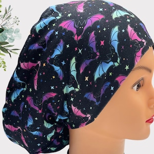 Puede incluir: Un gorro de quirófano negro con un estampado colorido de murciélagos y estrellas. El gorro está hecho de una tela suave y cómoda y es perfecto para enfermeras, médicos y otros profesionales de la salud.