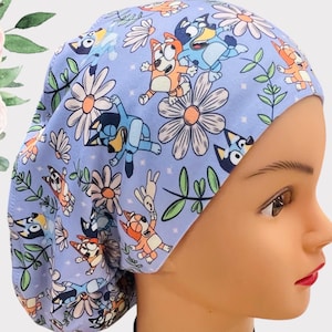 Puede incluir: Un gorro de quirófano azul con un estampado colorido de perros de dibujos animados y flores. El gorro está hecho de un tejido suave y transpirable y es perfecto para enfermeras, médicos y otros profesionales de la salud.