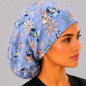 May include: A light blue scrub cap featuring a repeating pattern of cartoon dogs in various poses, interspersed with white daisy flowers and small green leafy sprigs. The fabric has a soft, rounded shape designed to cover the hair completely.