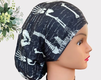 Op de afbeelding: Zwarte scrubcap met een witte anatomische skeletdiagram print. De tekst "TIMA'S SCRUB CAP" is gedrukt op de zijkant van de cap.