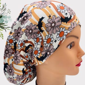 Puede incluir: Un gorro de trabajo blanco con un patrón floral marrón y naranja y murciélagos negros. El patrón presenta un estilo retro de los años 70.