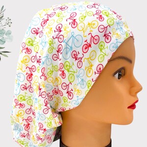 May include: A white scrub hat with a colorful bicycle print. The hat has a tie on the back.