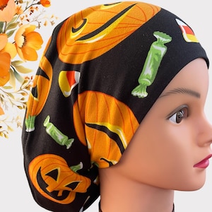 Może przedstawiać: Czarny czepek chirurgiczny z motywem Halloween. Czepek przedstawia pomarańczowe i czarne dynie, kukurydzę cukrową i cukierki na czarnym tle.