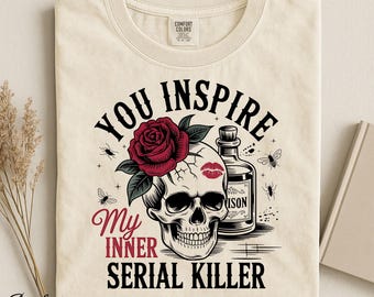 Op de afbeelding: Een ivoorkleurig t-shirt met een grafische print van een menselijke schedel versierd met een rode roos en een rode lippenstift kusafdruk. Naast de schedel staat een fles met het label POISON. De tekst luidt YOU INSPIRE MY INNER SERIAL KILLER.