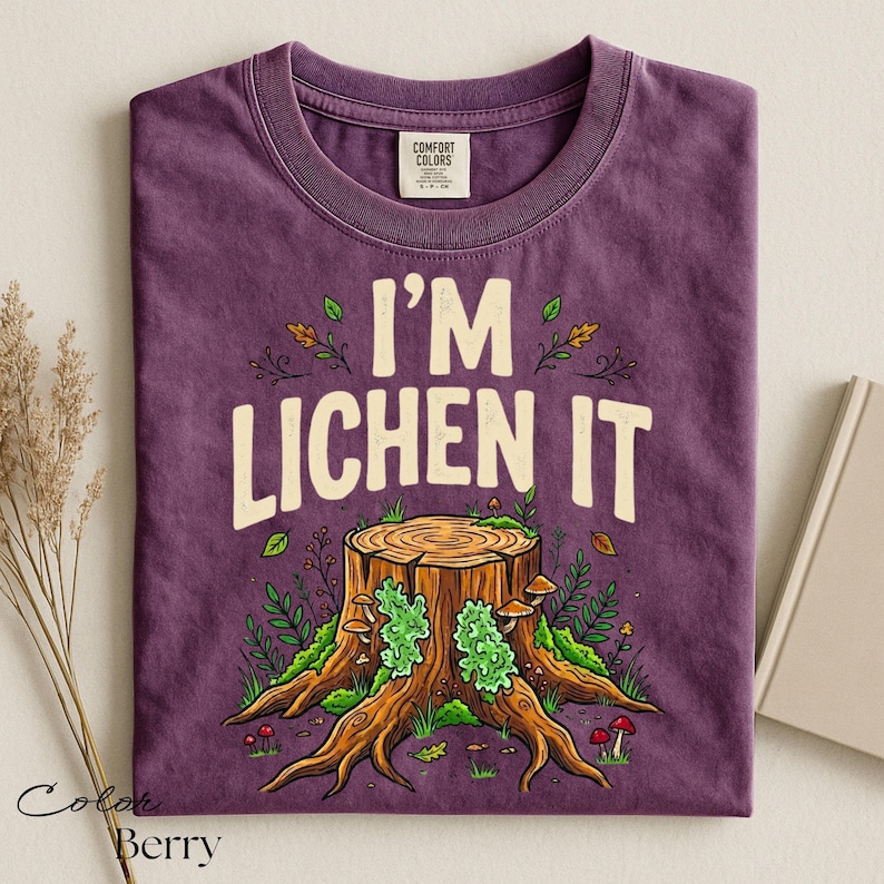 Puede incluir: Camiseta de color bayas con el texto "I'M LICHEN IT" sobre una ilustraci&oacute;n de toc&oacute;n de &aacute;rbol. El gr&aacute;fico presenta un toc&oacute;n de &aacute;rbol detallado con musgo verde, setas y follaje. La camiseta es de material Comfort Colors.
