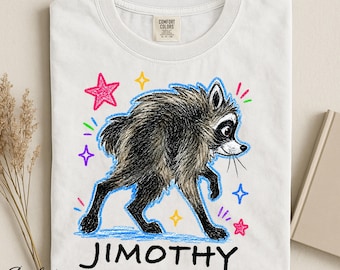 Op de afbeelding: Een wit t-shirt met een afbeelding van een harige wasbeer met zwarte en bruine vacht. De wasbeer is omringd door handgetekende sterren en streepjes in roze, geel, blauw en groen. De tekst JIMOTHY staat in het zwart eronder gedrukt.