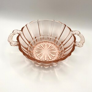 May include: A pink glass bowl with two handles. The bowl has a fluted design and a starburst pattern on the bottom.