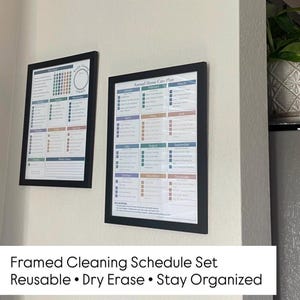 May include: Two framed cleaning schedule sets with black frames are mounted on a white wall. The schedules are colorful, with sections for each month and tasks. The text at the bottom reads: Framed Cleaning Schedule Set, Reusable, Dry Erase, Stay Organized.