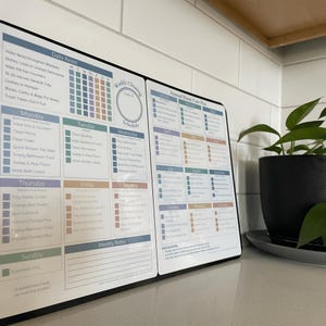 May include: A black and white cleaning schedule with sections for daily, weekly, and annual tasks. The schedule includes a daily reset checklist and a weekly cleaning schedule. A potted plant sits to the right.