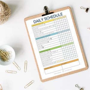 Puede incluir: Un portapapeles de madera con un horario diario impreso. El horario se divide en rutinas de mañana, después de la escuela y de la noche, con casillas de verificación para cada día. Clips dorados y una madeja de hilo están cerca. El texto dice 'Daily Schedule'.