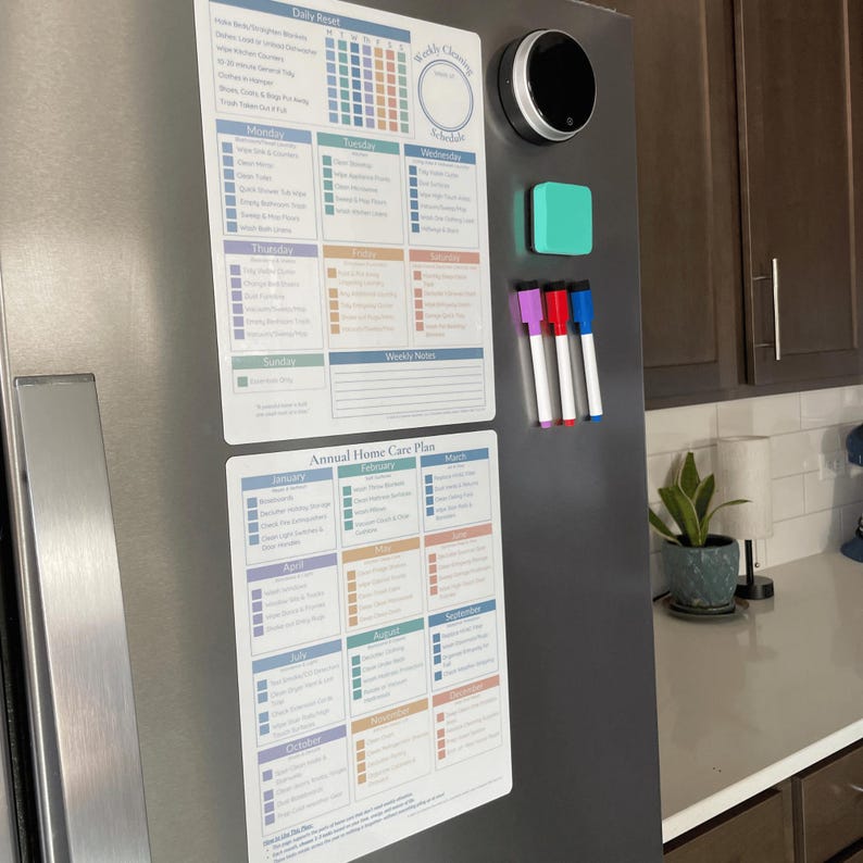 May include: A stainless steel fridge door features a magnetic weekly cleaning schedule, a daily reset checklist, and an annual home care plan. A smart home device, a small teal square, and three coloured dry-erase markers are also attached.