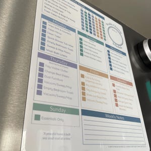 May include: A white magnetic cleaning schedule with a weekly layout. It features daily tasks, a calendar, and a section for weekly notes. The schedule includes tasks like cleaning the kitchen, bathrooms, and bedrooms.