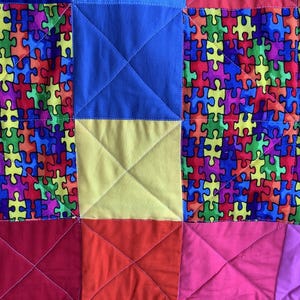 May include: A colorful quilt with a patchwork design featuring a variety of colors, including red, blue, yellow, pink, and green. The quilt is made up of squares with a puzzle piece pattern.