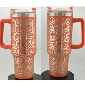 Puede incluir: Taza de viaje de acero inoxidable naranja con tapa y asa. La taza está cubierta con un patrón de caras de calabaza plateadas.