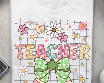 May include: White t-shirt with a colorful floral and grid design. The word "TEACHER" is displayed in a decorative font, with a green bow and pencil graphic at the bottom. Pink, white, and yellow flowers are scattered around the text.