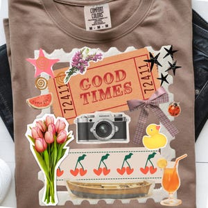 Peut inclure: T-shirt marron avec un motif collage comprenant un appareil photo vintage, un billet avec l'inscription "GOOD TIMES", des fleurs, des cerises, un bateau et un cocktail. Le t-shirt a une étiquette Comfort Colors.