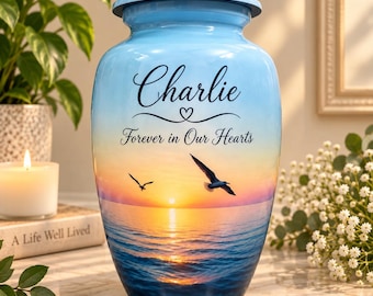 Könnte beinhalten: Eine hellblaue Urne mit einer Sonnenuntergangs-Meerszene und zwei fliegenden Möwen. Der Text "Charlie" ist in schwarzer Schrift über dem Satz "Forever in Our Hearts" aufgedruckt. Die Urne verfügt über einen passenden Deckel.