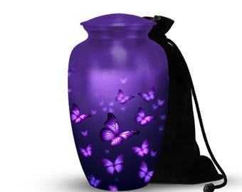 Puede incluir: Una urna morada con tapa a juego, adornada con un patrón de mariposas moradas. Una bolsa negra con cordón está al lado de la urna. La urna tiene un acabado liso y brillante.