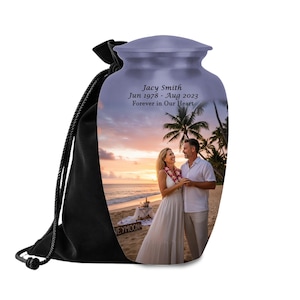 May include: A lavender-colored cremation urn with a photo of a couple on a beach at sunset. The urn has the inscription "Jacy Smith Jun 1978 - Aug 2023 Forever in Our Heart." It is presented with a black drawstring bag.