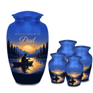 May include: A large blue cremation urn and four smaller matching urns, each featuring a sunset scene of a person fishing in a boat on a lake with mountains and trees. The text "IN LOVING MEMORY OF Dad" is printed in white on the front of each urn.
