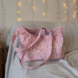 May include: A pink floral tote bag with a single strap. The bag is made of a soft, lightweight fabric and has a simple, casual design.