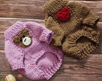 May include: Two knitted dog sweaters. One is lavender with a brown teddy bear face applique. The other is brown with a red heart applique. Both sweaters have sleeves and openings for the legs.