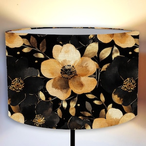 Puede incluir: Pantalla de lámpara ovalada con estampado floral. El diseño presenta grandes flores estilo acuarela en tonos dorados y negros, con detalles de hojas doradas, sobre un fondo negro. Ideal para una lámpara de mesa.