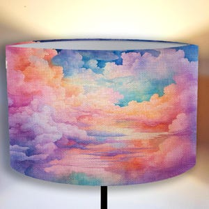 Puede incluir: Una pintura de acuarela de un cielo de puesta de sol con nubes esponjosas en tonos de rosa, morado, azul y naranja. Las nubes están superpuestas y crean una sensación de profundidad y dimensión. La pintura es perfecta para una pantalla de lámpara u otros fines decorativos.