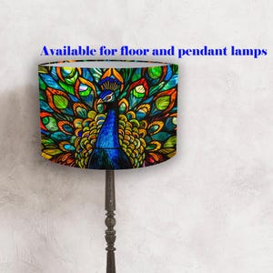 May include: A lampshade with a vibrant peacock design in shades of blue, green, and orange. The lampshade is cylindrical and is supported by a dark brown lamp stand. Text on the image reads: "Available for floor and pendant lamps."