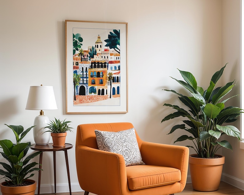 May include: A framed print of a colourful illustration of a cityscape with buildings and palm trees. The print is hanging on a white wall above an orange armchair with a patterned cushion. There are two potted plants in the room.