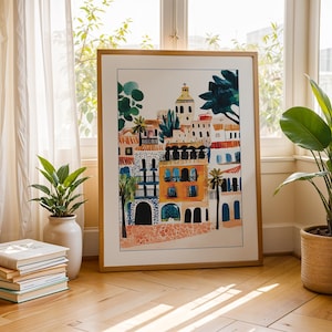 May include: A framed illustration of a colourful cityscape with buildings in shades of orange, yellow, and blue. The buildings have arched doorways and windows, and there are palm trees and other greenery in the foreground.