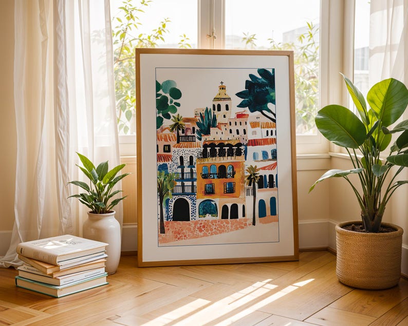 May include: A framed illustration of a colourful cityscape with buildings in shades of orange, yellow, and blue. The buildings have arched doorways and windows, and there are palm trees and other greenery in the foreground.
