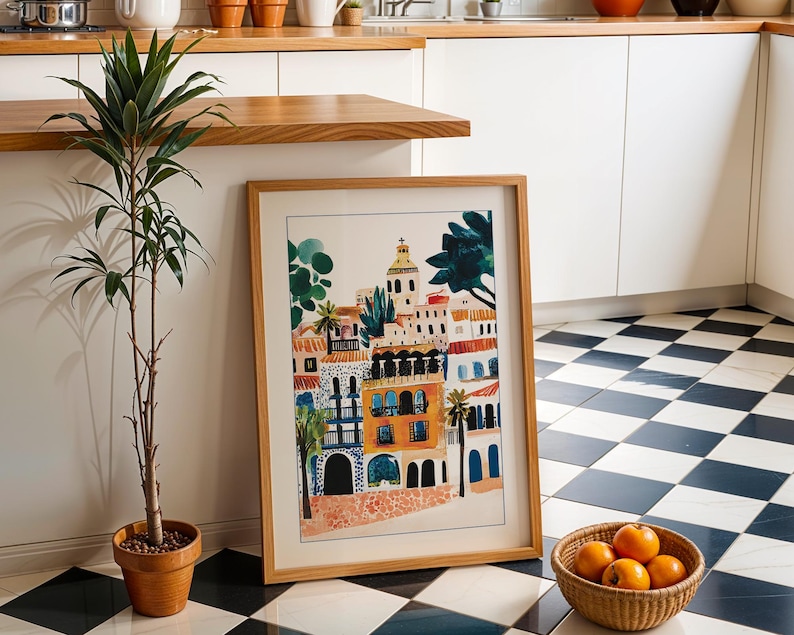 May include: A framed print of a colourful illustration depicting a cityscape with buildings, trees, and a blue sky. The print is in a wooden frame and is hanging on a white wall.